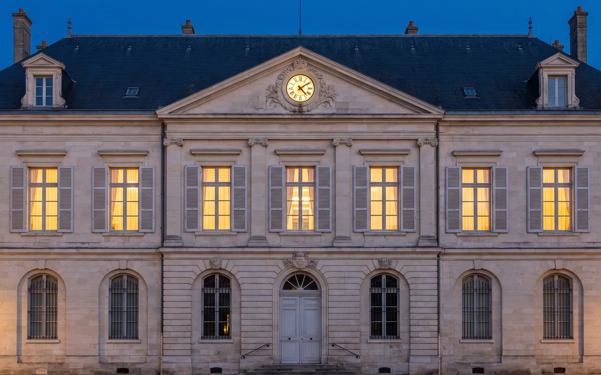Façade symétrique d’un hôtel de ville à l’heure bleue, fenêtres éclairées.